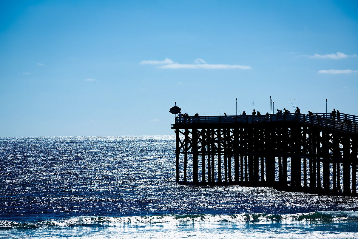 Pier extending into the ocean with people on it against a clear blue sky.