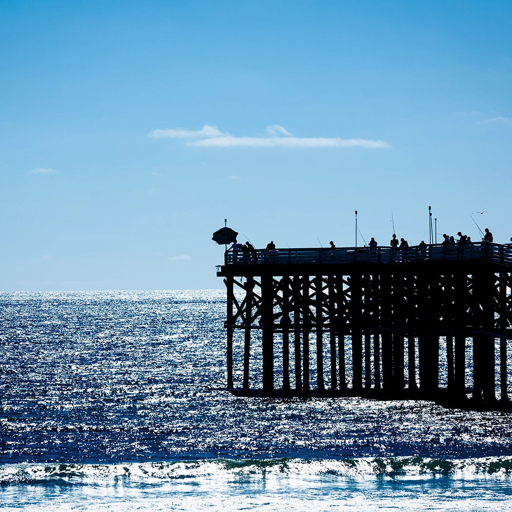 Silhouette of a pier with people against a clear blue sky over the ocean.