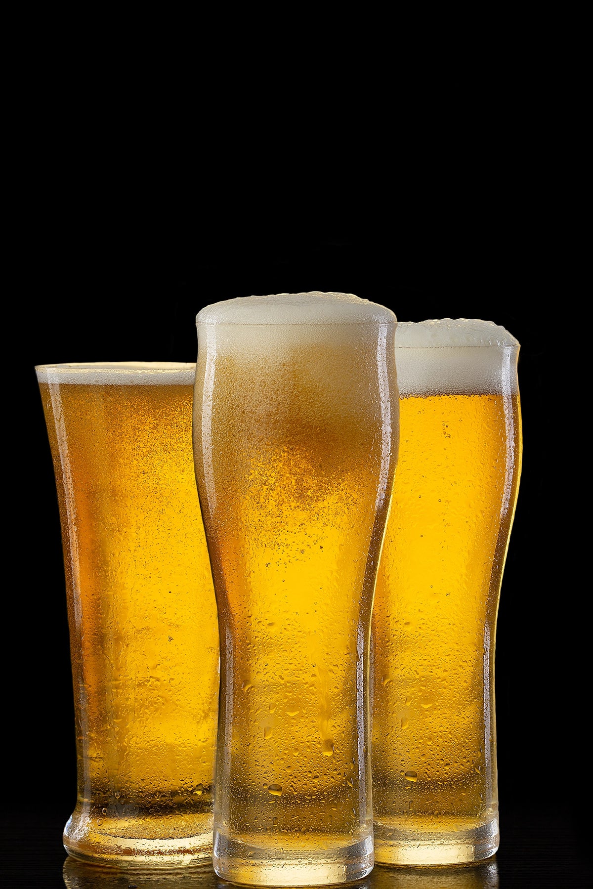 Three glasses of beer with foam on a black background