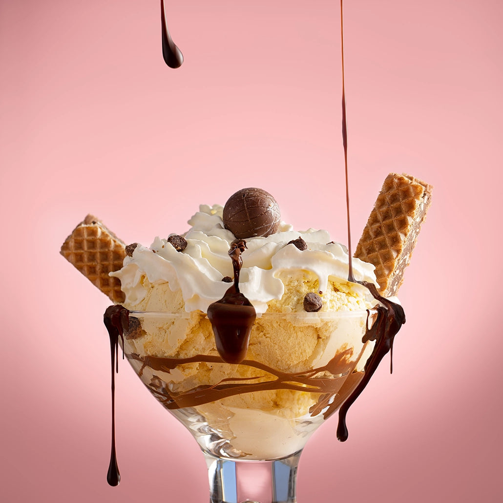 Ice cream sundae with waffles, chocolate drizzle, and a pink background