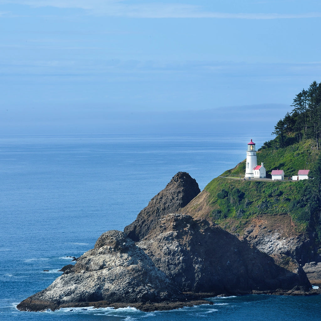 Lighthouse on a rocky cliff overlooking the ocean with clear blue sky.